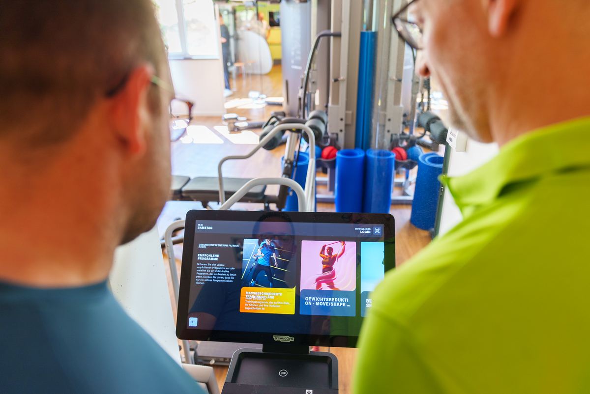 Ein Trainer des Gesundheitszentrums Dentl zeigt einem Mitglied den Trainingsplan auf dem Bildschirm am Gerät